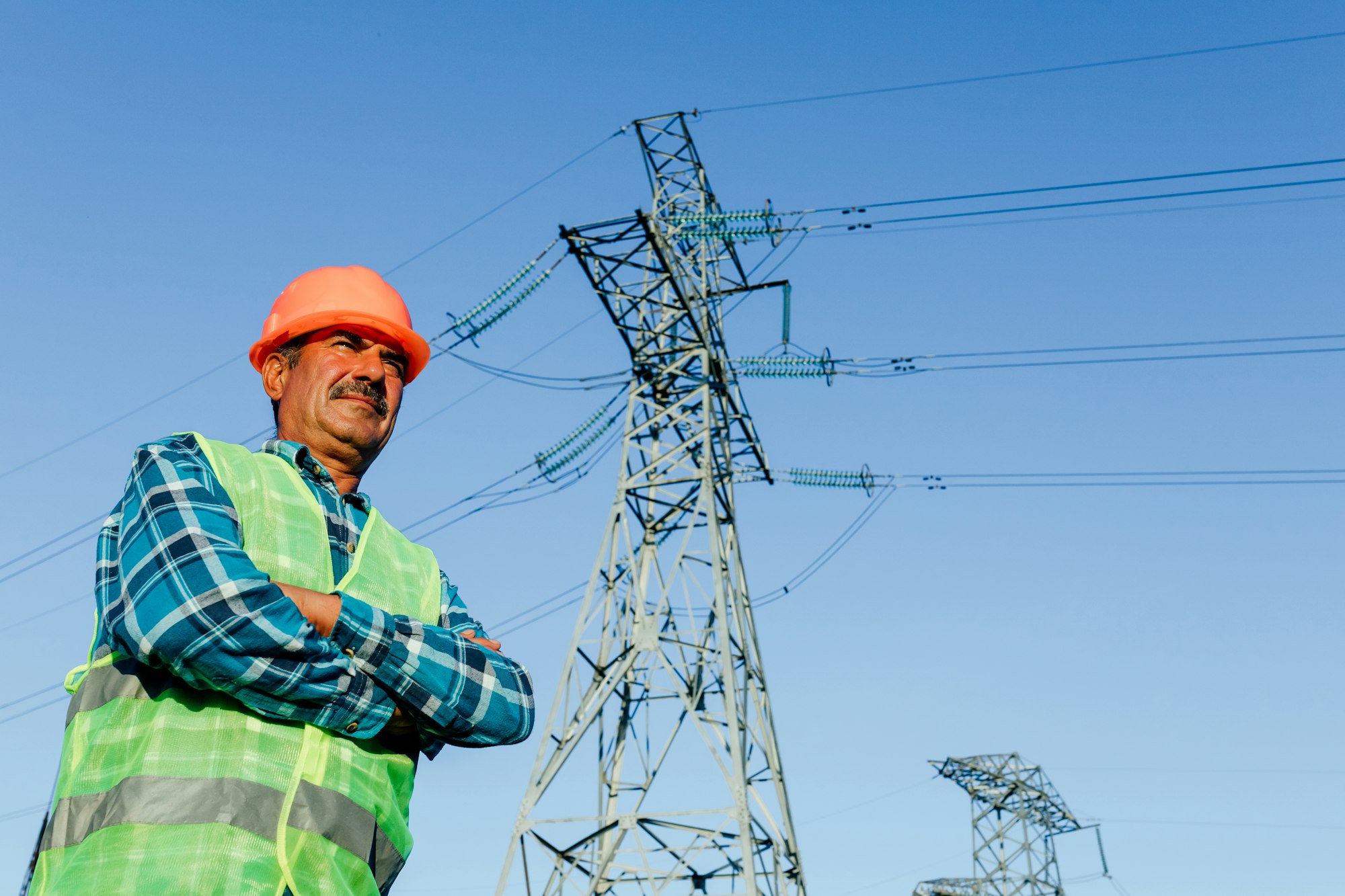 Confident male worker standing against industrial electric poles